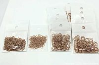 Multiple small clear plastic bags each containing rose gold plated jump rings of varying sizes, shown in group packed for lot display.