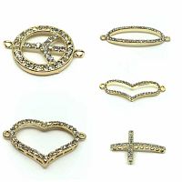 Five distinct gold-plated jewelry connector charms each decorated with clear Czech crystals, depicting peace sign, cross, hollow heart, oval, and chevron shapes.
