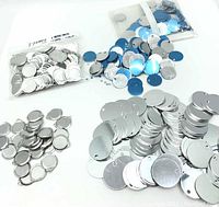 Top view of mixed round aluminum blanks in various groups with protective blue film on some and bezel rimmed blanks in a bag.