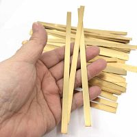 Hand holding three rectangular brass strips against pile of similar strips representing bracelet blanks