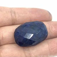 Hand holding large faceted oval sapphire bead, showing faceted surfaces and texture