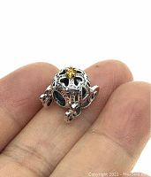 Photo showing the pumpkin carriage charm on fingers for scale, highlighting the gold crown and detailed silver body with stones.