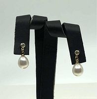 Pair of drop-shaped freshwater pearl earrings displayed on a black earring holder. Pearls are white with notable lustre, attached to CZ studs and gold-plated brass fittings.
