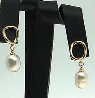 Pair of earrings displayed on black stand showing oval-shaped white freshwater cultured pearls hanging from small irregular shaped gold plated brass posts.