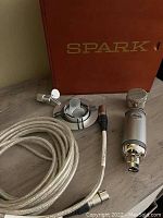 Blue Spark condenser microphone with shock mount, cable, and red storage box on wooden surface
