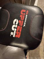 Close up of the Bowflex Upper Cut machine's padded seat with logo in red and white on black.