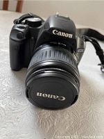 Front-angle view of camera body with attached lens and cap, strap visible