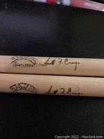 Close-up image showing two natural wood Vic Firth drumsticks with Eagles logo and Scott F. Crago's signature printed.