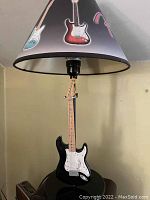 Lamp showing black Fender Stratocaster guitar replica base and cone lampshade with guitar designs