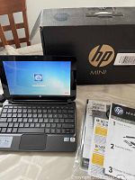 Open HP Mini 210 netbook powered on next to original box and manuals