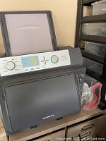 Side and front view showing the printer with lid open, control panel and paper tray, branded Olympus.