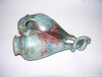 Side angle showing the double spouted bulbous pottery with blue and red glaze, twisted handle, and textured surface.