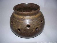 Front angle view of brown glazed ceramic jar with round holes