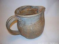 Side view of rustic ceramic pitcher showing handle, speckled glaze and pouring lip.