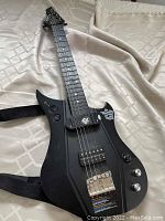 Black electric guitar controller viewed from top angle, showing frets, bridge, strap, and control buttons