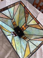 Top-down photo showing interior geometric stained glass panels in shades of green, brown, yellow, and amber framed in dark metal.