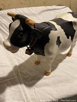 Front side view of the vintage black and white cow figure showing its detailed face, tan horns, red collar with small bell, and body markings.