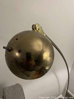 Close-up of the brass spherical lampshade showing ventilation holes and adjustment joint.