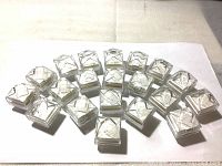 Top view of 20 new clear acrylic jewelry boxes arranged on a surface, showing transparent faceted lids and cushioned inserts inside.