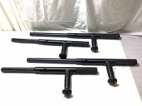 Four black extendable police tonfa batons with textured grip side handles, laid flat showing various lengths.