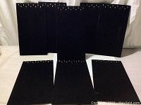 Front view of eight black velvet jewelry display panels arranged upright, showing multiple golden hooks at the top of each panel for hanging jewelry.
