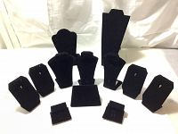 Full set of black velvet jewelry display stands arranged on white surface, showing a variety of shapes and sizes for necklaces, earrings and rings.