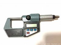 Full view of the digital micrometer showing measuring spindle, thimble, and LCD display along with function buttons.
