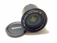 Front view of Sigma Zoom 28-300mm f/3.5-6.3 Macro lens part showing front glass element and Sigma lens cap beside it.