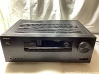 Front view of the Onkyo black AV receiver showing digital display, control buttons, power button, and large volume knob.