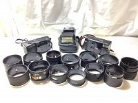 Two vintage film cameras (Kodak S900 Tele and VR35 Medalist) with 12 assorted lens hoods laid out in front, mostly black, various sizes and internal shapes.