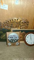 Photo showing carved wooden fish art, square clock with mountain photo, round clock, and a rectangular metal plaque with embossed mountain and figure.