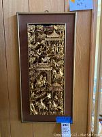 Front view of gold-tone carved Asian wall art panel in frame