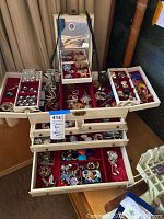 Overall view of open cream-colored jewelry box with trays and drawers filled with assorted costume jewelry