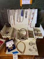 Complete view of the jewelry box open with various jewelry items displayed including necklaces, earrings, brooch, and multiple compartments of the box.