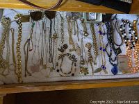 Wide view of assorted costume jewelry laid out on towel showing necklace chains, bracelets, brooches, pendants and rhinestone sunglasses.