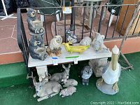 Wide view of assorted animal statues under and on garden bench: bear planter, owl, rabbit, deer family, pelican, duck, turtle, and small bust.