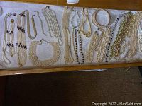 Full display of assorted pearl and costume jewelry including multiple necklaces arranged horizontally on white fabric.