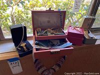 Photo shows an assortment of watches, costume jewelry, and a pink wooden jewelry box on a windowsill with natural light.