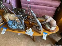 Wide shot showing all five wildlife sculptures arranged on a wooden mid-century modern table against a pink upholstered chair and other furniture.