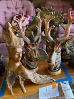 Photo of assorted wildlife sculptures including two deer busts with antlers, an abstract wooden figure, and a brass or bronze moose sculpture.