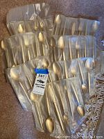 Flatware set stored in satin-like fabric rolls, showing multiple utensils including spoons, forks, knives.