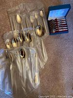 Photo of gold tone serving spoons and forks laid out on soft white cloth and carpet, showing variety of spoon sizes and fork pieces.