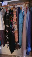 Closet view showing a row of ladies sweaters, including various knit styles and colors hanging on wooden hangers.