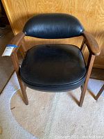 Front view of black leather cushioned MCM arm chair showing the seat, backrest, and wooden arms.