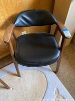 Front view of black vinyl and wood Mid-Century Modern armchair showing the padded seat and backrest, with curved wooden armrests.