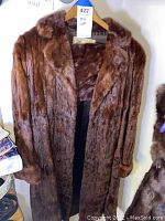 Front view of the brown mink fur coat hanging on a hanger showing full length, collar, sleeves, and lining