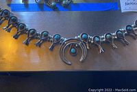 Full view of necklace laid flat showing central Naja pendant and squash blossoms on silver bead chain