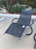 Side view of black mesh fabric patio lounger with curved black and silver tubular frame showing overall shape and design.