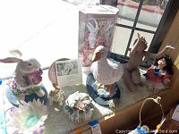 Wide photo showing lot items together including porcelain doll, Lladro rabbit statuette, ceramic rabbits, plastic goose, glass bowl.