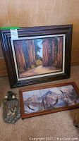 Three pieces of decor including a framed forest landscape painting, a framed mountain eagle scene, and a carved eagle wall hanging.
